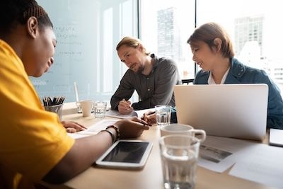 Three people sitting at a table with electronic devices